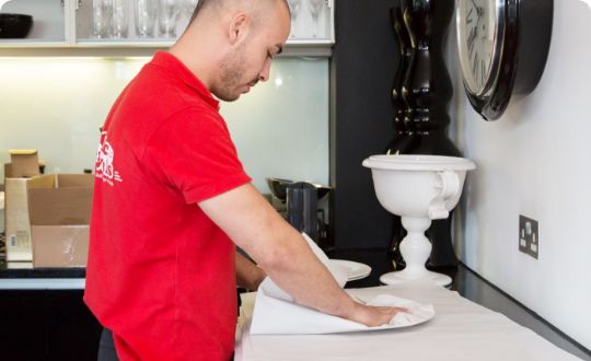 The image shows a removals specialist who is packing white porcelain plates in boxes.
